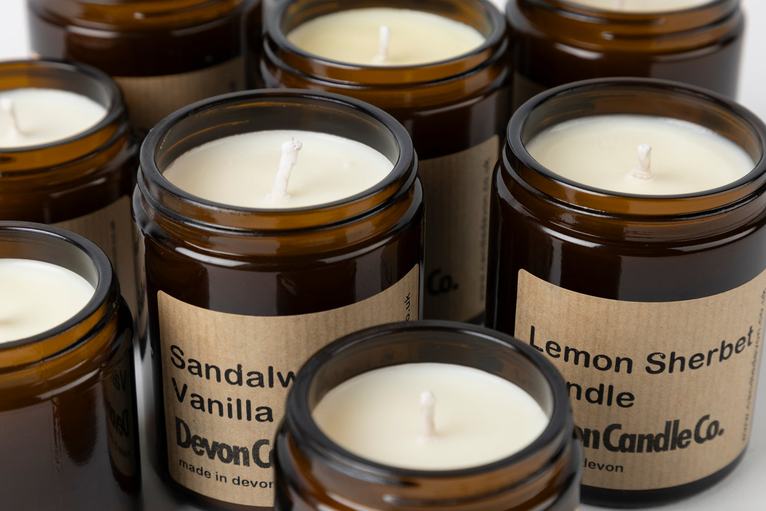 Six Devon Candle Co. soy-wax candles in amber apothecary jars with kraft labels printed sandalwood vanilla and lemon sherbet, made in devon
