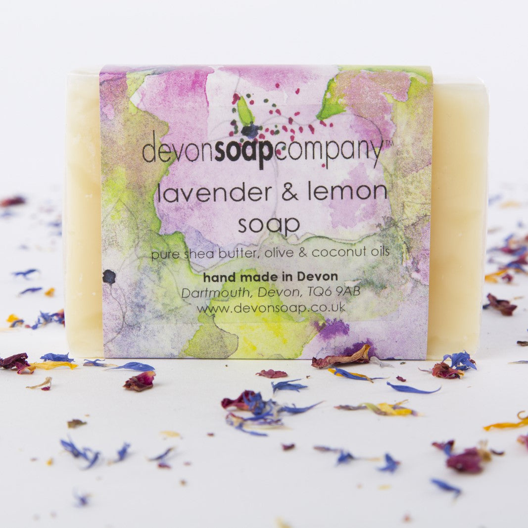 Lavender and Lemon soap bar wrapped in a pink, yellow and green watercolour label printed with the words pure shea butter, olive and coconut oils, hand made in Devon, Dartmouth, Devon TQ6 9AB, with scattered cornflower and rose petals